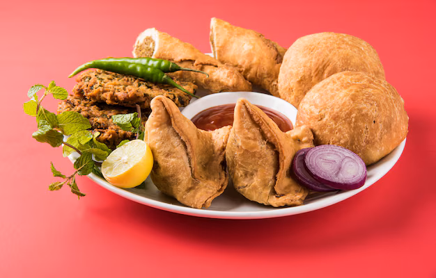 Crispy samosa and kachori served hot with green chutney and tamarind sauce on a plate.